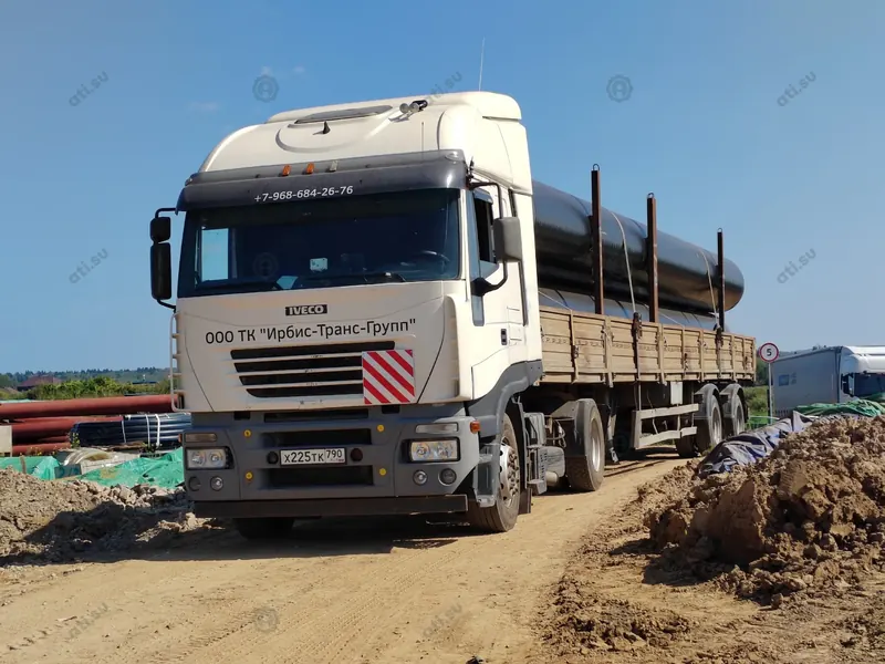 Тягач Iveco с длинномерными стальными трубами на строительной площадке