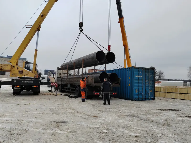 Крановая погрузка труб большого диаметра рядом с контейнерной площадкой
