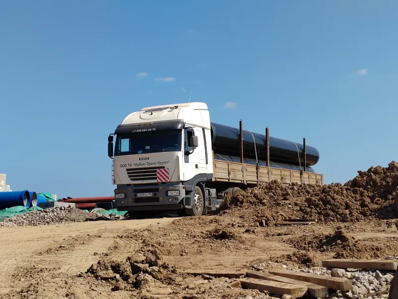 Тягач Iveco с длинномерными трубами на грунтовой строительной площадке