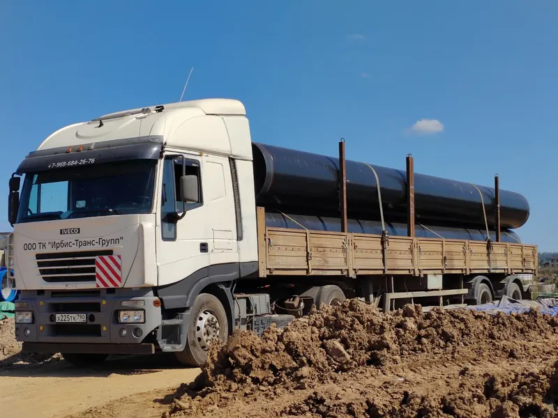 Тягач Iveco с трубами большого диаметра на земляной площадке
